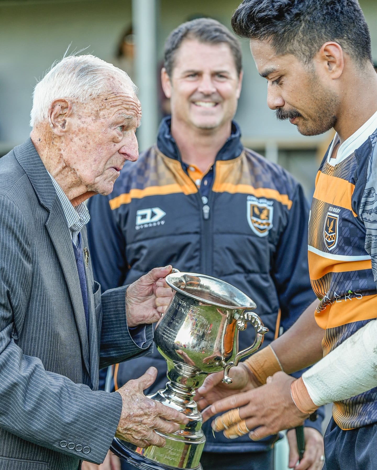 A club life member presenting the cup to an Eden Rugby player